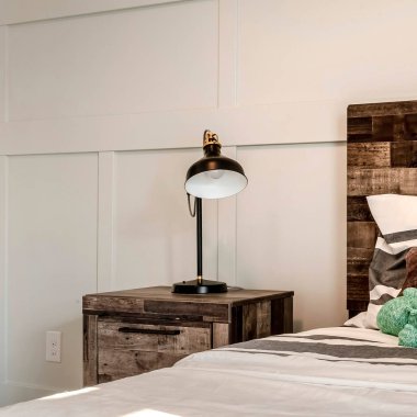 Kahverengi ahşap karyola başlıklı tek kişilik yatak ve modern lambalı yan masa.