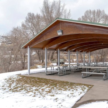 Kışın karla kaplı parkın ortasında tavanında ahşap kemerler olan kare Pavilion.