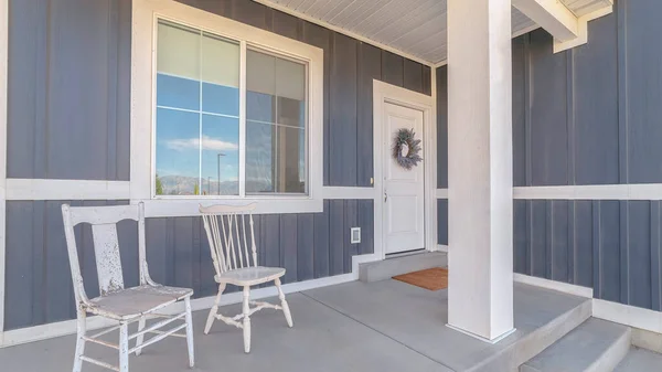 Panorama White porch chairs against window and front door of home with gray exterior wall