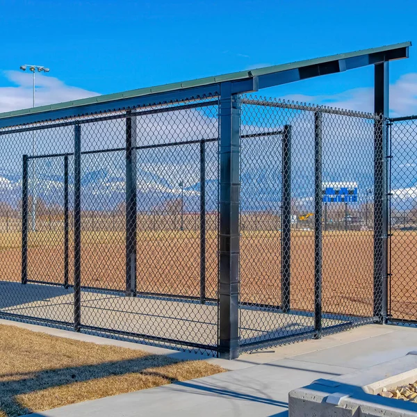 Square crop Baseball field dugout with slanted roof and chain link fence on a sunny day