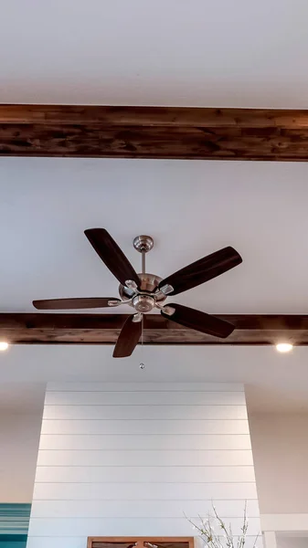 Vertical Ceiling fan with lights between decorative wood beams inside living room of home