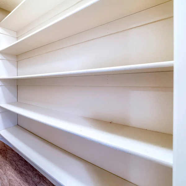 Square crop Small walk in closet with empty long cabinet shelves under slanted ceiling — Stock Image Square crop Small walk in closet with empty long cabinet shelves under slanted ceiling Royalty Free Stock Images