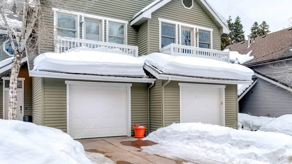 Panorama Facade of home with snowy driveways in front of two car garage viewed in winter