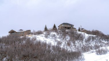 Panorama ekin tepesi. Evleri ve yumuşak yamacında yapraksız çalıları kışın karla kaplı.