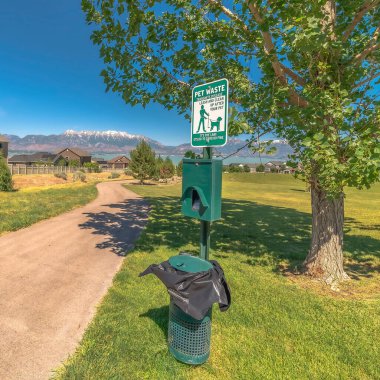 Kare Hayvan Atık İstasyonu Ağaç ve patikanın yanında köpek dışkısı torbaları ve çöp tenekesi