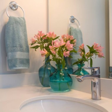 Kare lavabo ve paslanmaz çelik musluk beyaz tezgahın üstünde vazolarda çiçeklerle