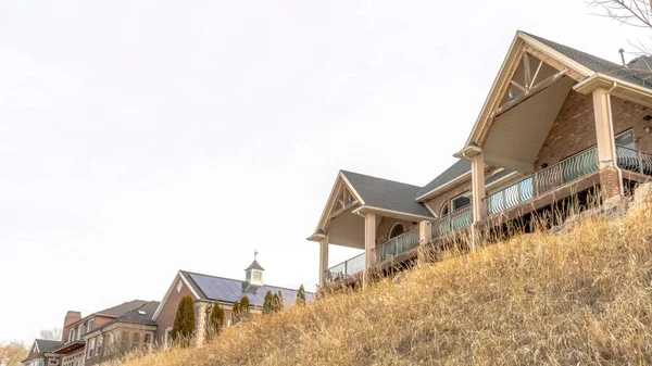 Panorama Beautiful houses sitting on top of grassy slope beneath sky filled with clouds