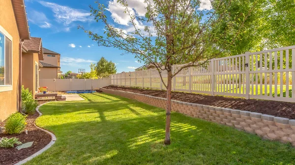 Panorama frame Home backyard with vibrant lawn and raised planting bed along white picket fence