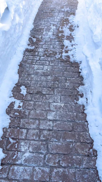 Vertikální rám Uzavření cesty dlážděné šedými kamennými cihlami uprostřed hluboké vrstvy čerstvého sněhu — Stock fotografie