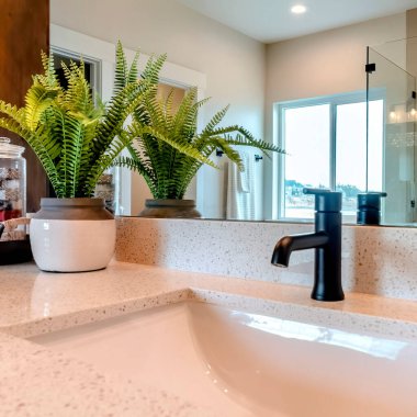 Kare lavabo ve musluk, duş kabinini ve kayan pencereyi yansıtan aynaya karşı