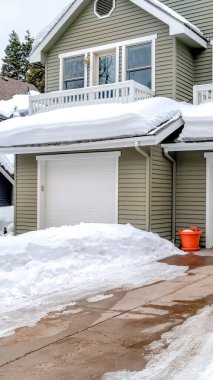 Vertical frame Facade of home with snowy driveways in front of two car garage viewed in winter clipart