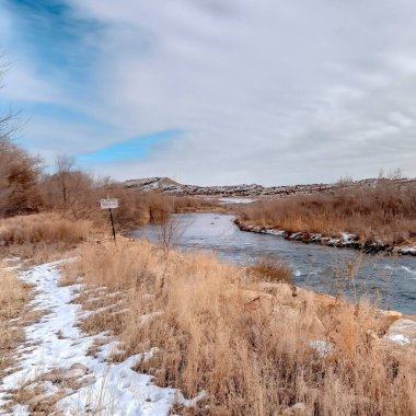 Kare ekin nehri. Çimenli ve kayalık kıyılar boyunca akan sular. Kış karıyla kaplanmış.