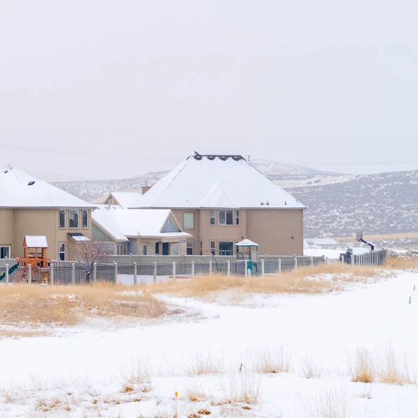 Casas cuadradas en la comunidad residencial cubierta de nieve contra la colina y el cielo nublado — Foto de Stock