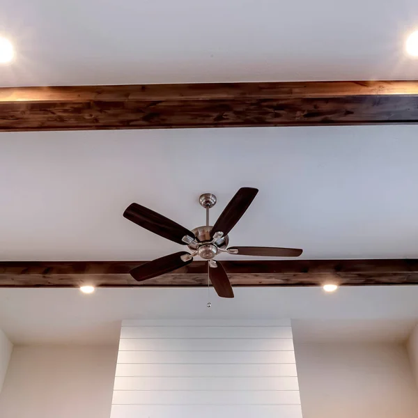 Square frame Ceiling fan with lights between decorative wood beams inside living room of home