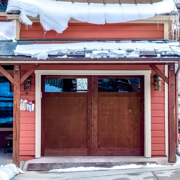 Square Brown wooden glass panelled garage door of home under snowy roofs in winter Stock Picture