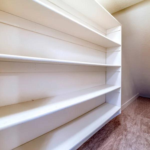 Square Small walk in closet with empty long cabinet shelves under slanted ceiling — Stock Image Square Small walk in closet with empty long cabinet shelves under slanted ceiling Royalty Free Stock Photos