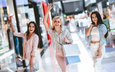 Üç çekici genç kızlar modern alışveriş merkezinde alışveriş torbaları ile alışveriş yapıyoruz.