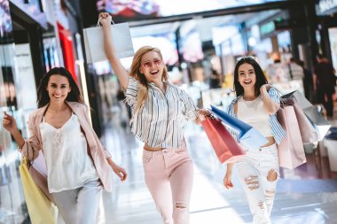 Üç çekici genç kızlar modern alışveriş merkezinde alışveriş torbaları ile alışveriş yapıyoruz.