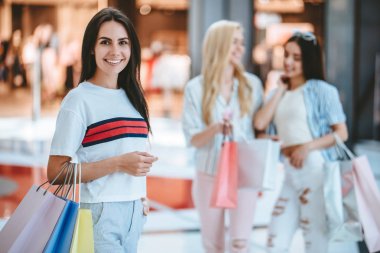 Üç çekici genç kızlar modern alışveriş merkezinde alışveriş torbaları ile alışveriş yapıyoruz.