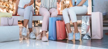 Üç çekici genç kızların kırpılmış görüntü modern alışveriş merkezinde alışveriş torbaları ile alışveriş yapıyoruz.