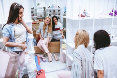 Üç çekici genç kız ayakkabı deposunda modern alışveriş merkezinde alışveriş torbaları ile alışveriş yapıyoruz.