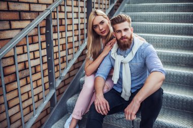 Genç şık mutlu çift zaman açık havada birlikte geçiriyor. Çekici kadın ve yakışıklı sakallı adam merdivenlerde şehirde oturuyor.