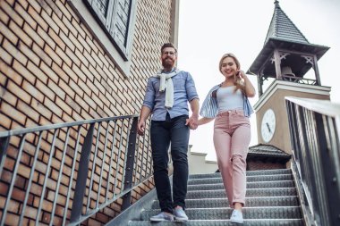 Genç şık mutlu çift zaman açık havada birlikte geçiriyor. Çekici kadın ve yakışıklı sakallı adam şehirde merdivenlerde yürüyor.