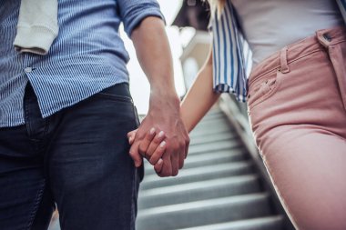 Çekici genç mutlu çiftin kırpılmış görüntü zaman açık havada birlikte geçiriyor. Şık çift Close-up merdivenlerde yürüyen ve elele.