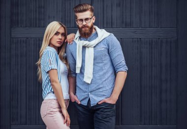 Şık genç çift zaman açık havada birlikte geçiriyor. Çekici kadın ve sakallı yakışıklı siyah ahşap arka plan üzerine poz.