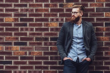 Şık sakallı adam tuğla zemin şehrin üzerine poz. Genç adam izole göz gözlük.