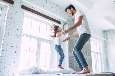 Seni seviyorum, baba! Yakışıklı genç adam evde küçük şirin kızı ile eğleniyor ve yatağın üstüne atlama. Mutlu babalar günü!