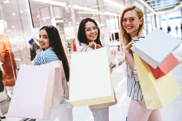 Üç çekici genç kızlar modern alışveriş merkezinde alışveriş torbaları ile alışveriş yapıyoruz.