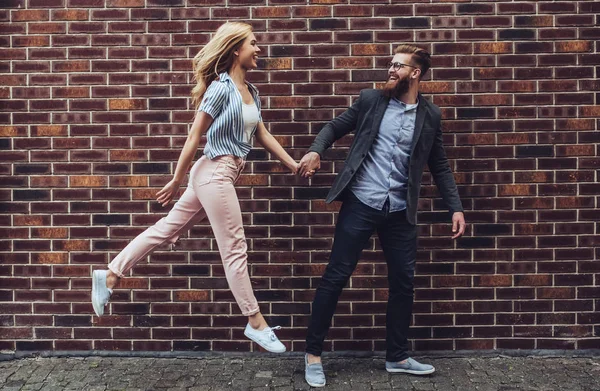 时髦的年轻夫妇在户外花时间 漂亮的女人和英俊的胡子男子走在砖背景和手牵着手 — 图库照片