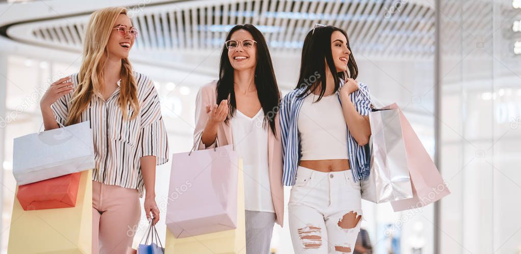 Three attractive young girls are doing shopping with shopping bags in modern mall.