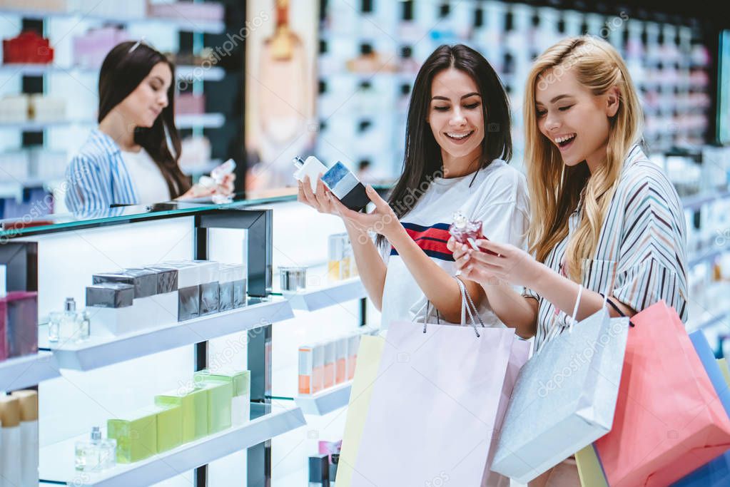 Three attractive young girls are doing shopping with shopping bags in perfume store in modern mall.