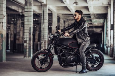 Klasik tarzı siyah motosiklet ile yakışıklı sakallı motorcu. Cafe yarış garaj içinde.
