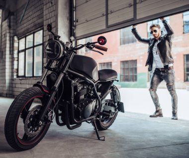 Klasik tarzı siyah motosiklet ile yakışıklı sakallı motorcu. Cafe yarış garaj içinde.