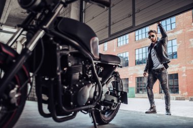 Klasik tarzı siyah motosiklet ile yakışıklı sakallı motorcu. Cafe yarış garaj içinde.