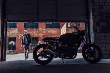 Klasik tarzı siyah motosiklet ile yakışıklı sakallı motorcu. Cafe yarış garaj içinde.