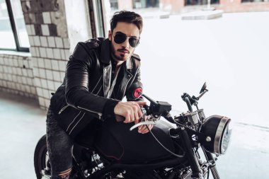 Klasik tarzı siyah motosiklet ile yakışıklı sakallı motorcu. Cafe yarış garaj içinde.