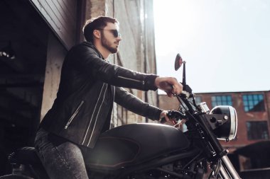 Klasik tarzı siyah motosiklet ile yakışıklı sakallı motorcu. Cafe yarış garaj içinde.