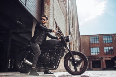 Klasik tarzı siyah motosiklet ile yakışıklı sakallı motorcu. Cafe yarış garaj içinde.