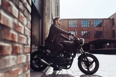 Klasik tarzı siyah motosiklet ile yakışıklı sakallı motorcu. Cafe yarış garaj içinde.