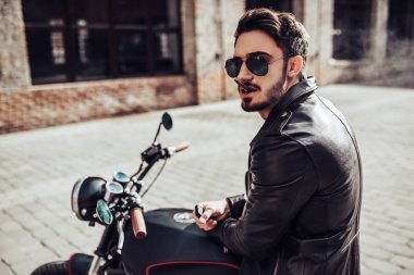 Yakışıklı sakallı motorcu klasik tarzı siyah motosiklet üzerinde otururken yasaktır sigarette var. Cafe racer.
