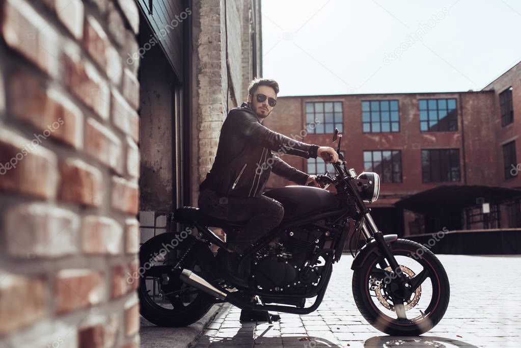 Handsome bearded biker with classic style black motorcycle. Cafe racer in garage.