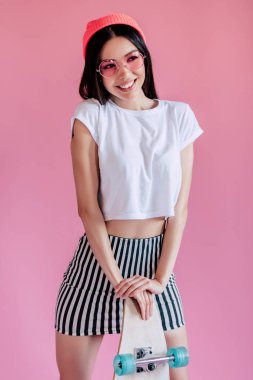 Genç Asyalı Genç kız pembe bir arka plan üzerinde. Şık patenci kız izole kaykay ile.