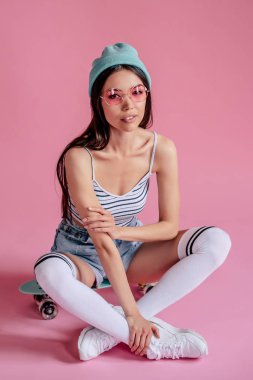 Pembe pembe gözlüklü Genç Asyalı Genç kızı. Patenci kız şort izole kaykay ile.