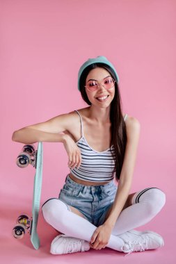 Pembe pembe gözlüklü Genç Asyalı Genç kızı. Patenci kız şort izole kaykay ile.