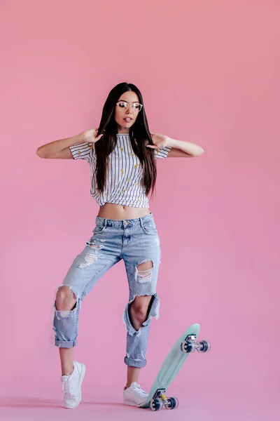 ピンクの背景に若いアジアの 代の少女 分離のスケート ボードとスタイリッシュな若い女性 — ストック写真