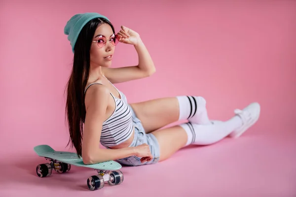 年轻的亚裔少女粉红色的背景粉红色的眼镜 滑板女孩在短裤与滑板隔离 — 图库照片